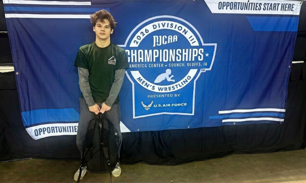Wrestler Zach Gomer standing by sign that reads NJCAA Champpionsips at the national tournament.